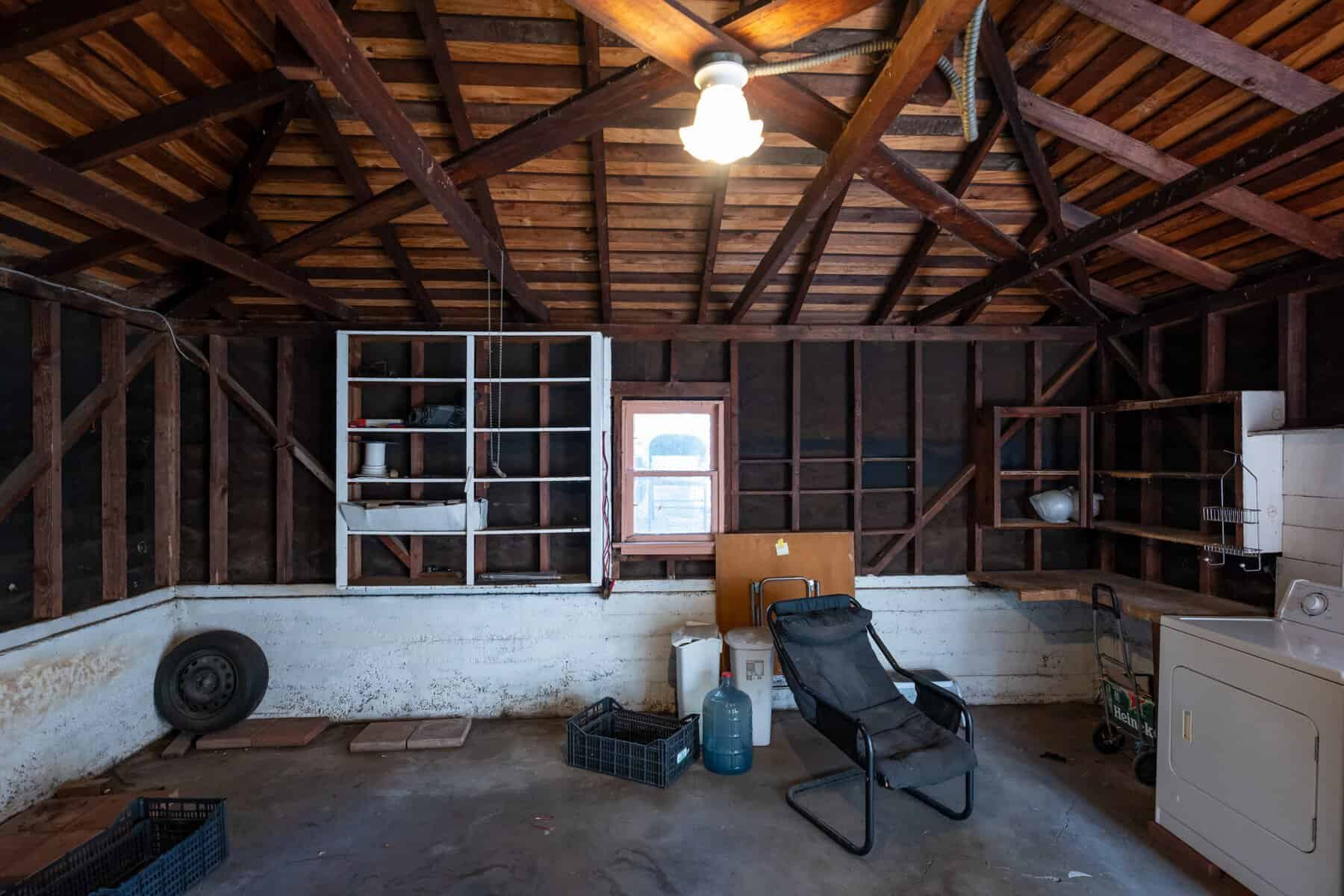 Old garage with exposed beams, unfinished walls, and scattered storage items