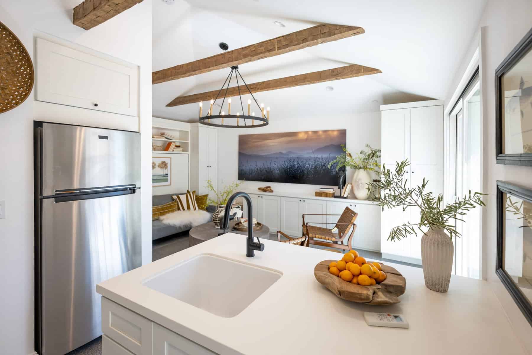 Bright kitchen-living space with wood beams, stainless fridge, and island with citrus centerpiece