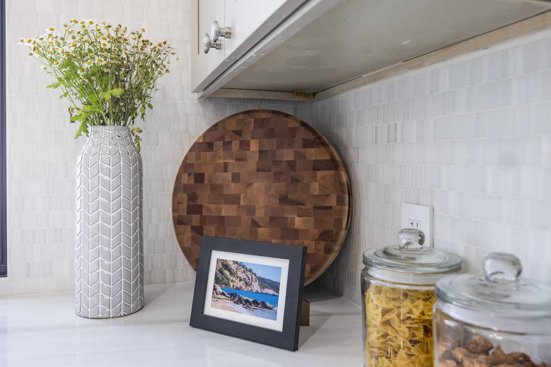 Kitchen counter with a vase, cutting board, photo frame, and jars.