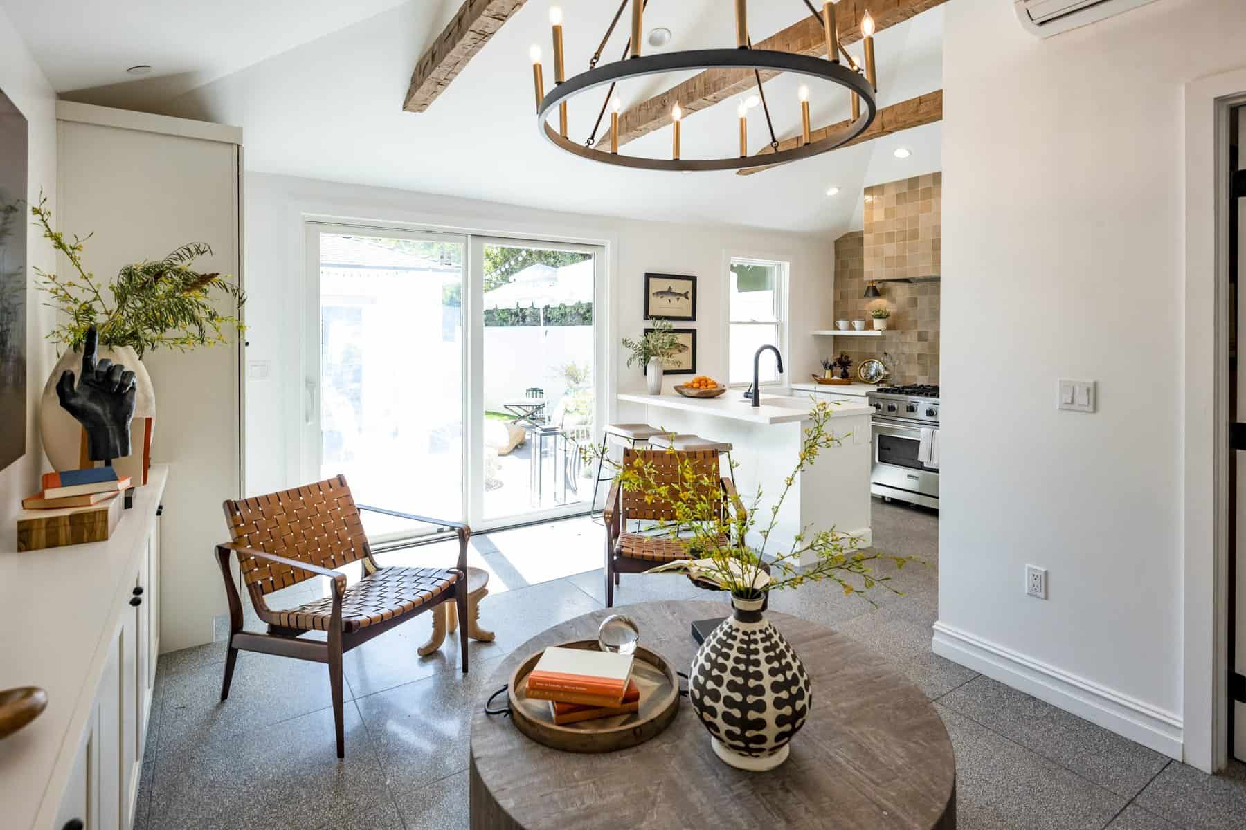 Open-concept kitchen and living space with a round wooden table, woven leather chairs, and a modern chandelier