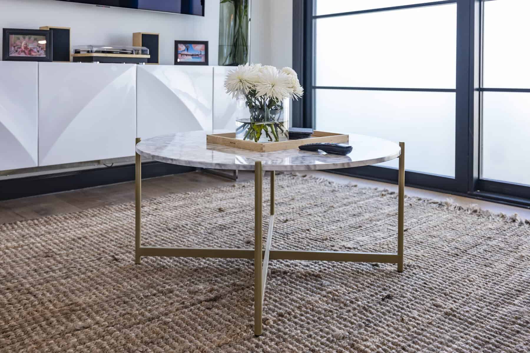 Modern living room with round marble coffee table, woven rug, and white flowers in a glass vase