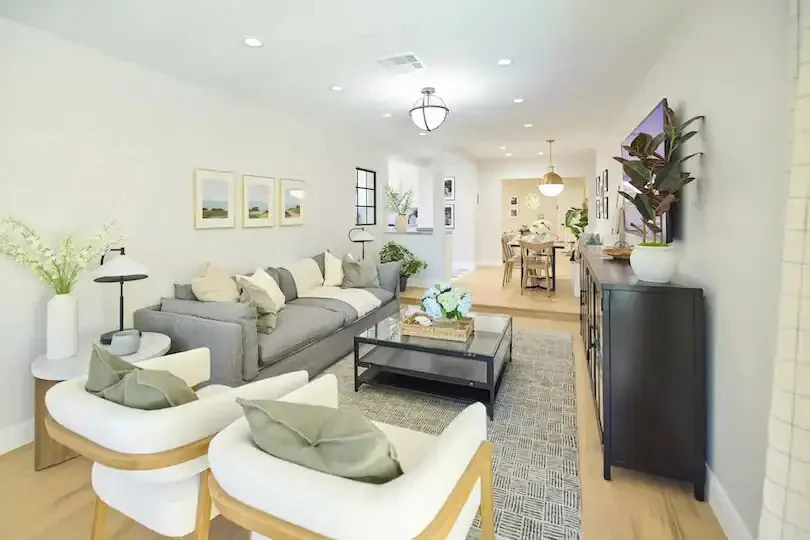 Bright living room with gray sofa, white chairs, and dining area