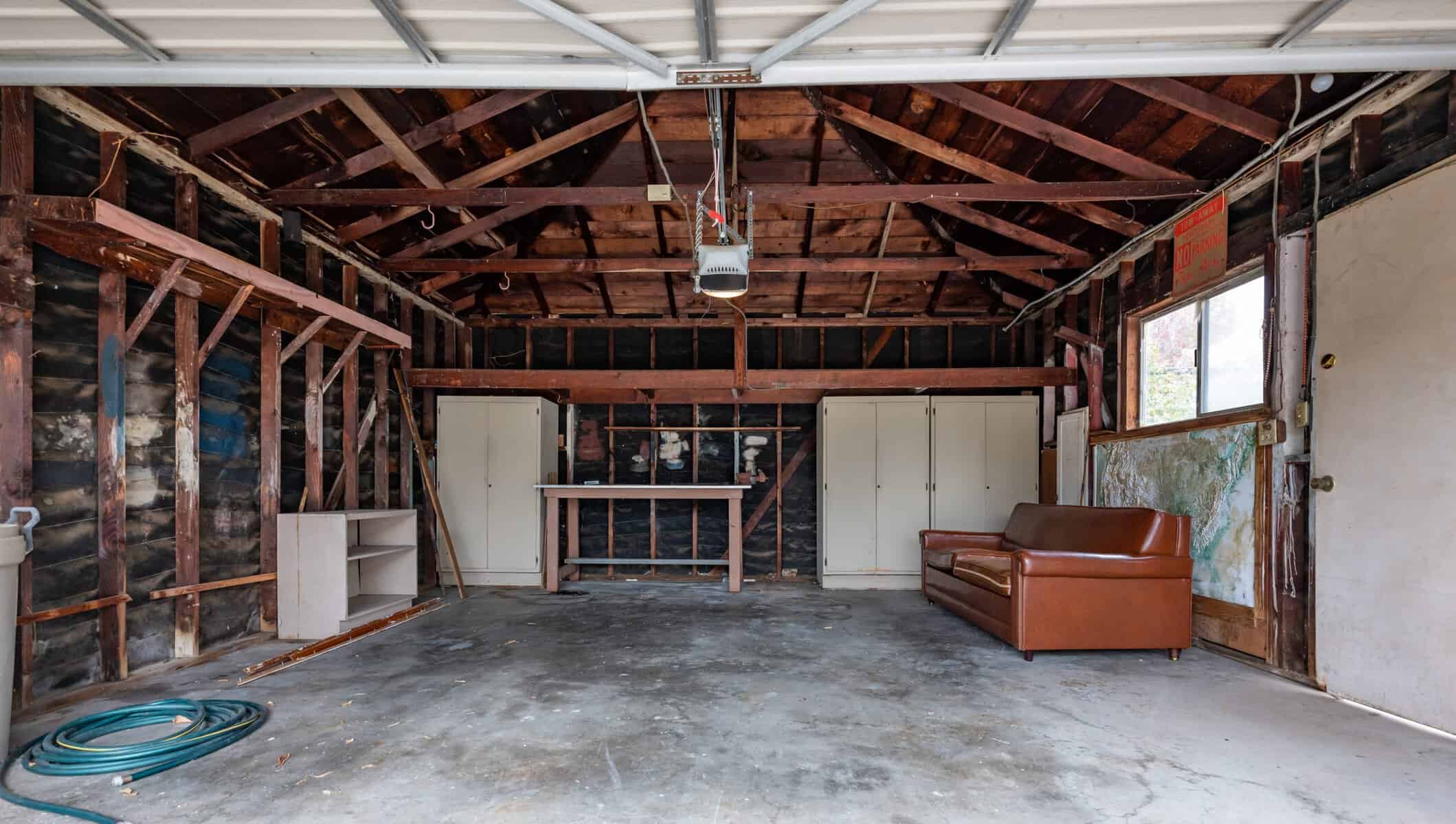 Rustic garage with exposed wooden beams, storage cabinets, and a brown leather couch