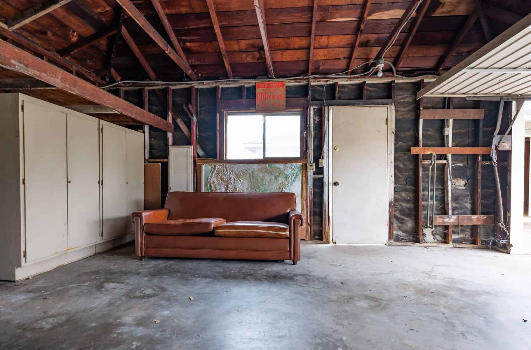 Unfinished garage with exposed beams, leather couch, and storage cabinets