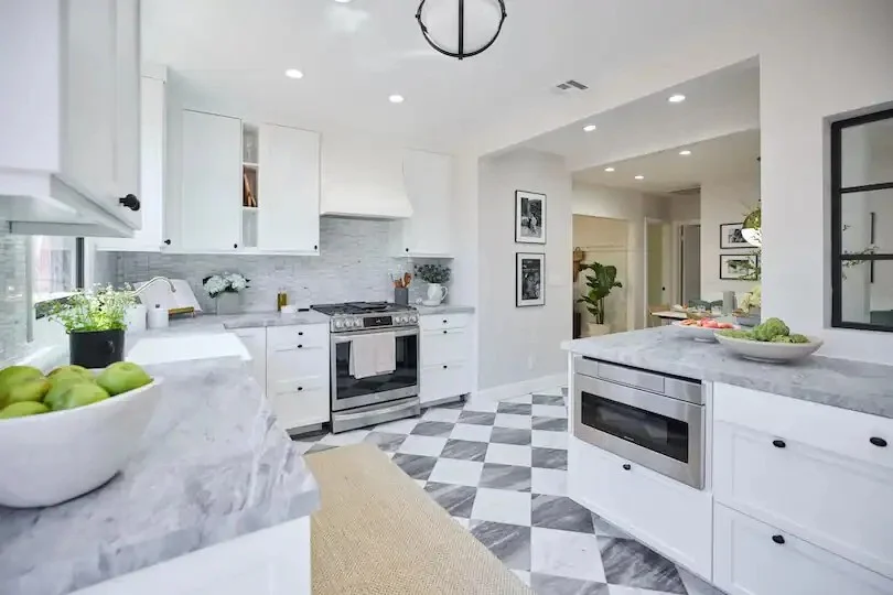 White kitchen with marble counters, checkered floors, and stainless steel appliances