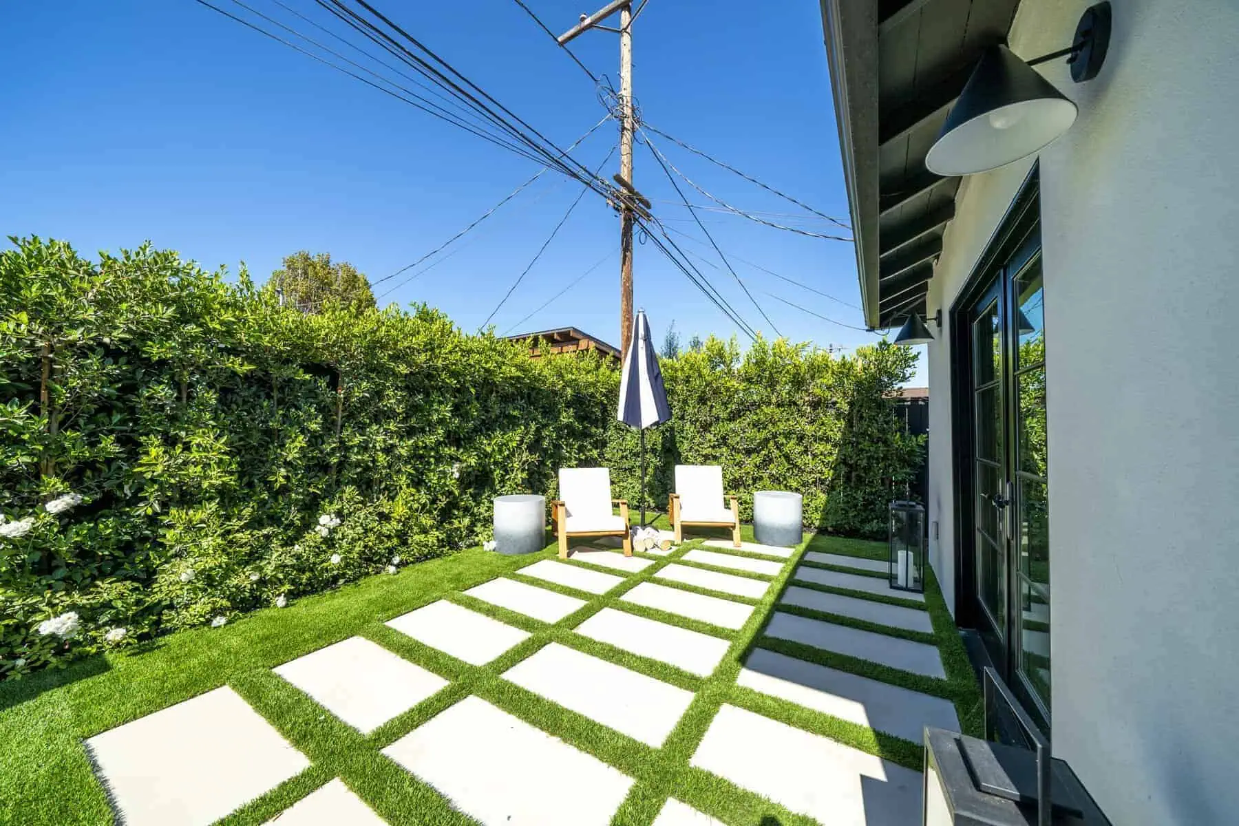 Backyard patio with pavers, chairs, and hedge fence
