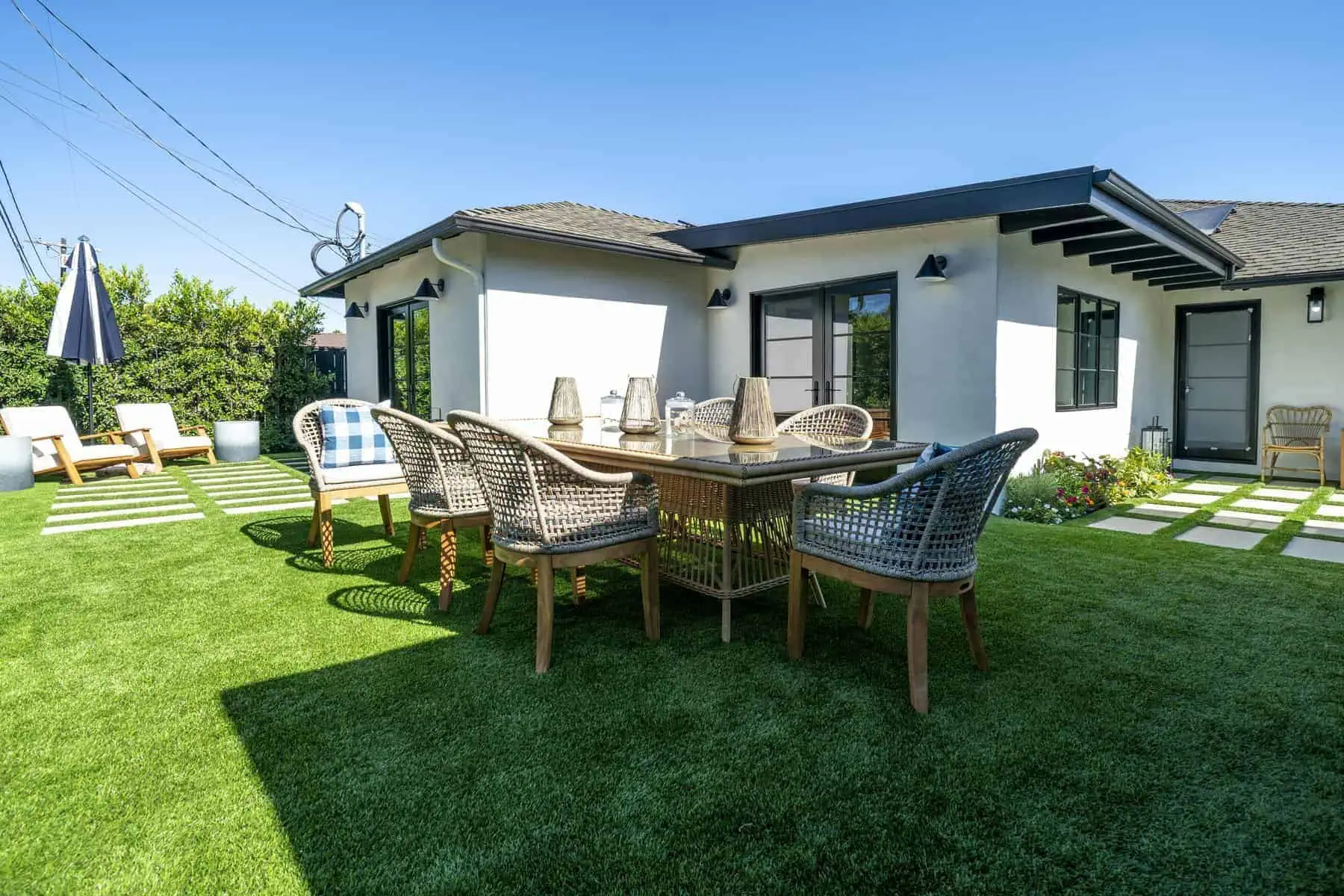 Backyard with artificial grass, wicker dining set, lounge chairs, and white modern house exterior