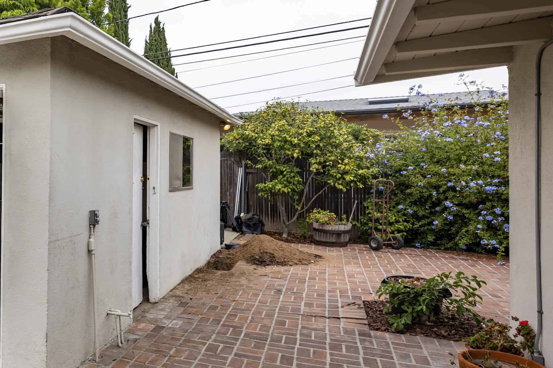 Brick patio with garden plants, storage shed, and a pile of soil