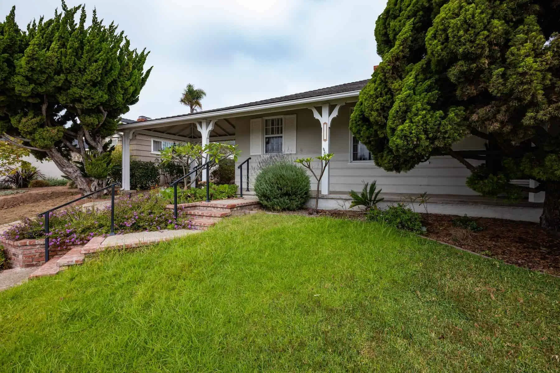 Single-story house with a front porch, brick steps, and well-maintained landscaping
