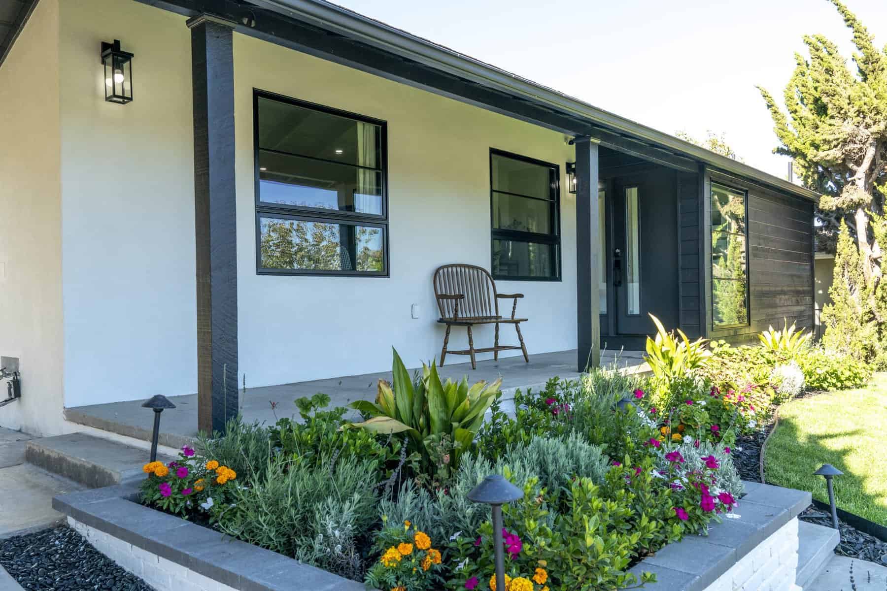 Modern house exterior with front porch, wooden bench, and colorful garden beds