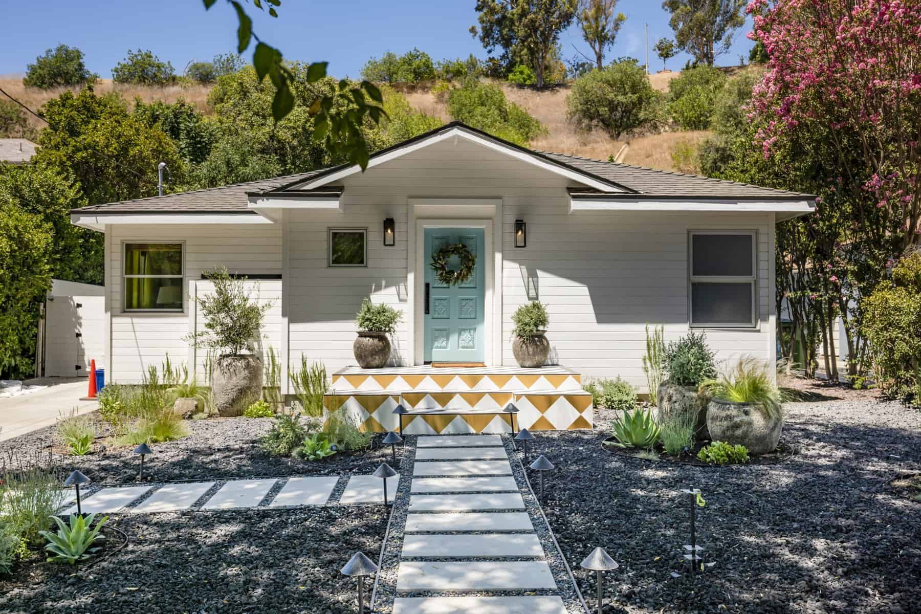 Front entrance with a blue door, geometric-patterned steps, and a gravel walkway with potted plants