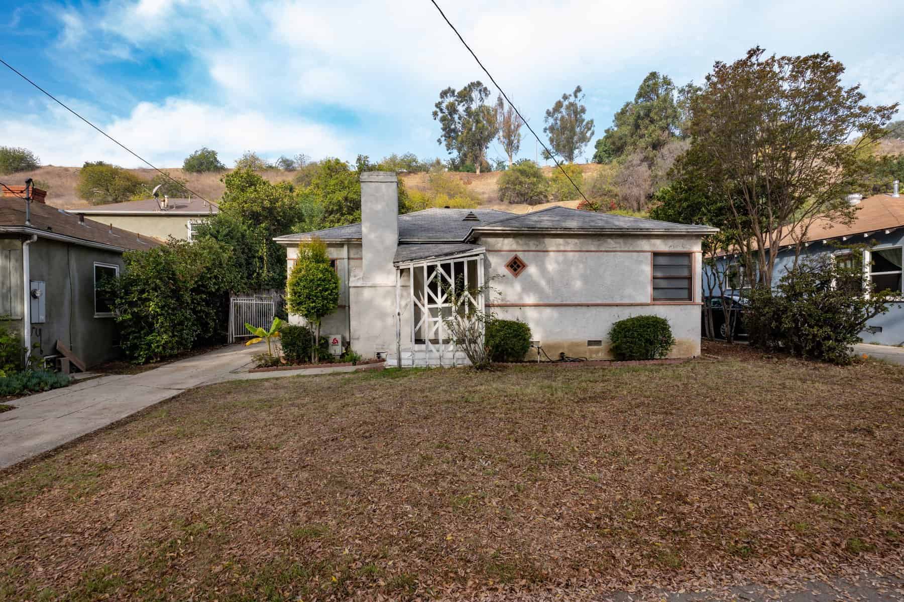 Small older home with a weathered exterior, front porch, and dry front lawn