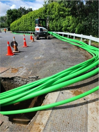 Heavy duty green conduit pipes installed for underground cable trenching on road.