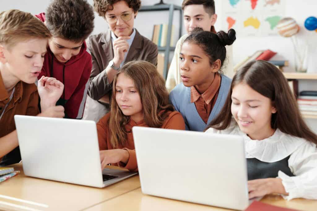 Niños pequeños usando laptops en clase mientras una docente los acompaña, aprendiendo con tecnología