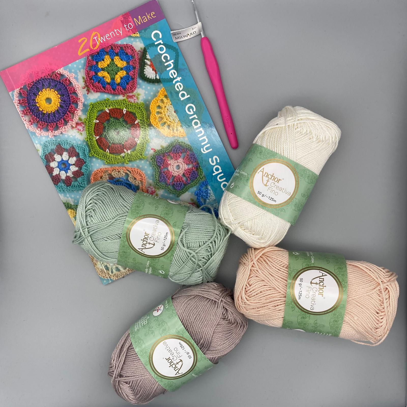 Vibrant crochet yarns and a colourful granny square crochet pattern book displayed on a grey surface, perfect for crafting and knitting projects.