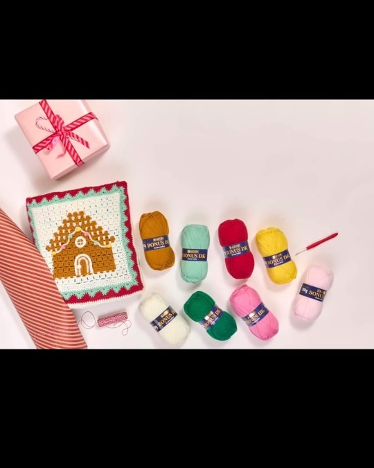 Colourful yarn balls and a festive crochet gingerbread house kit arranged on a white background, perfect for DIY sewing and craft projects available at Fabric & Finery.