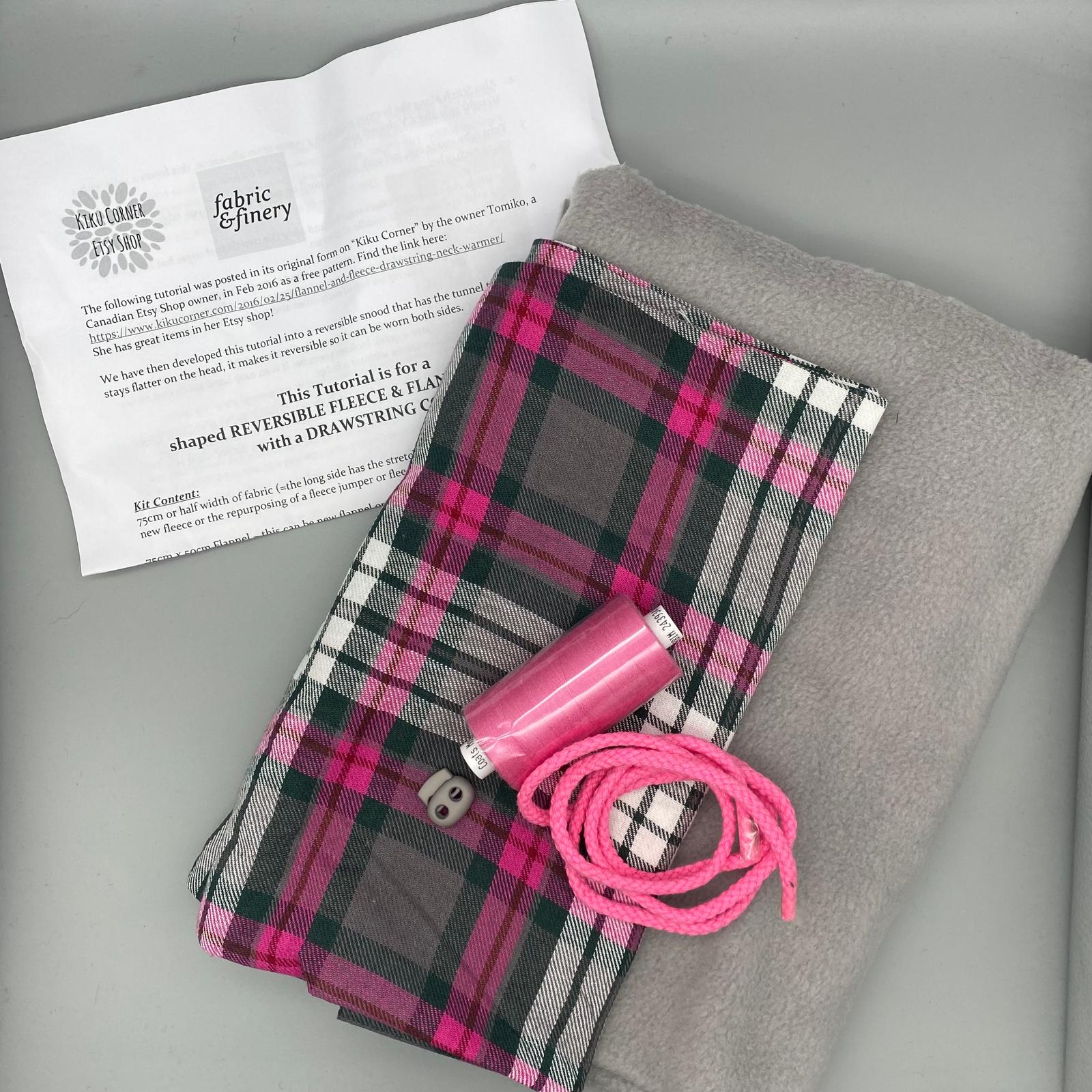 Pink and grey tartan fabric swatch with matching pink cord, sewing thread, and fleece, suitable for creating reversible fleece and flannel garments, available at Fabric & Finery.