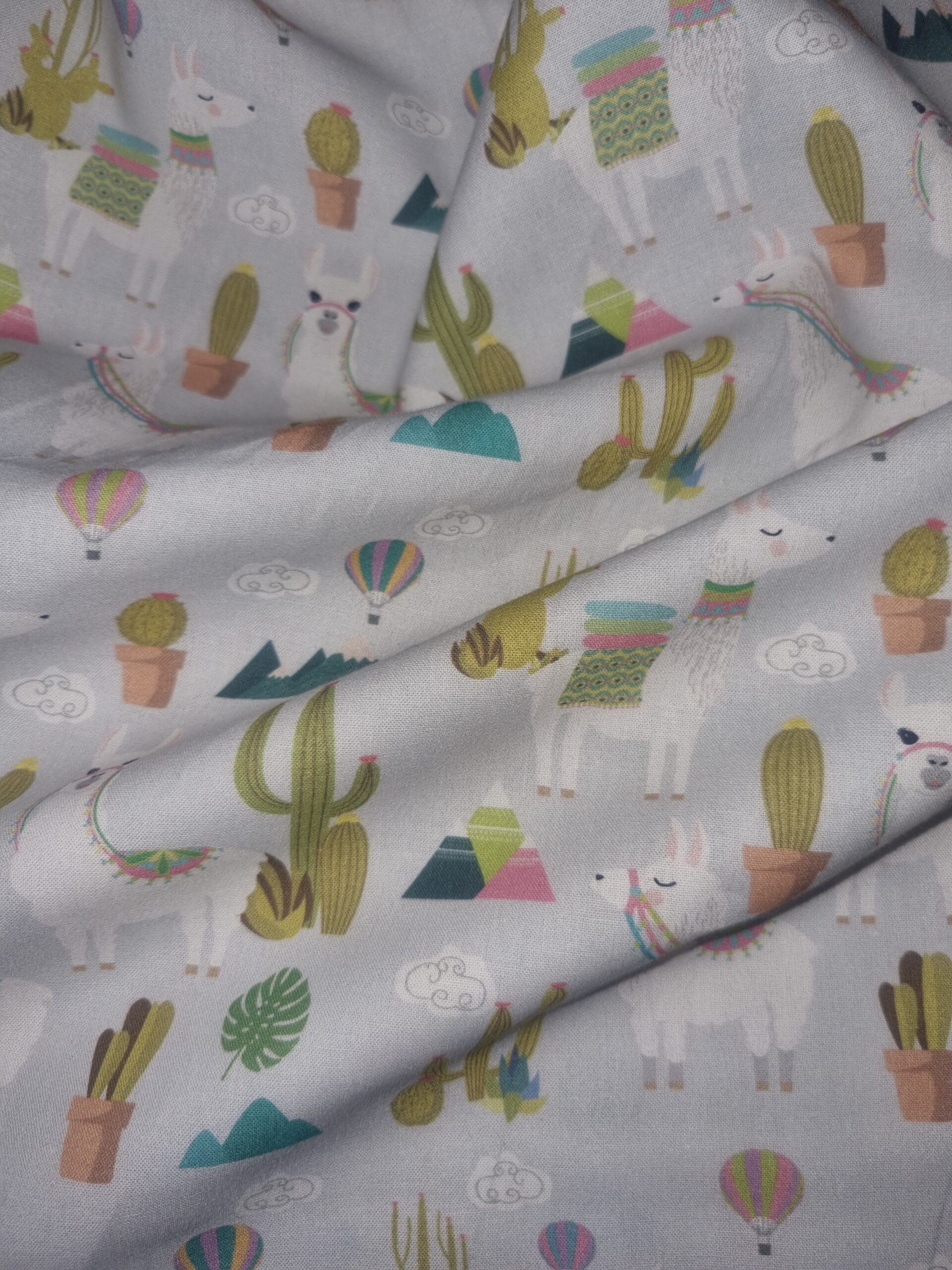 Vibrant llama and cactus printed fabric in pastel colours, perfect for trendy home decor, craft projects, and children's clothing, available at Fabric & Finery UK.