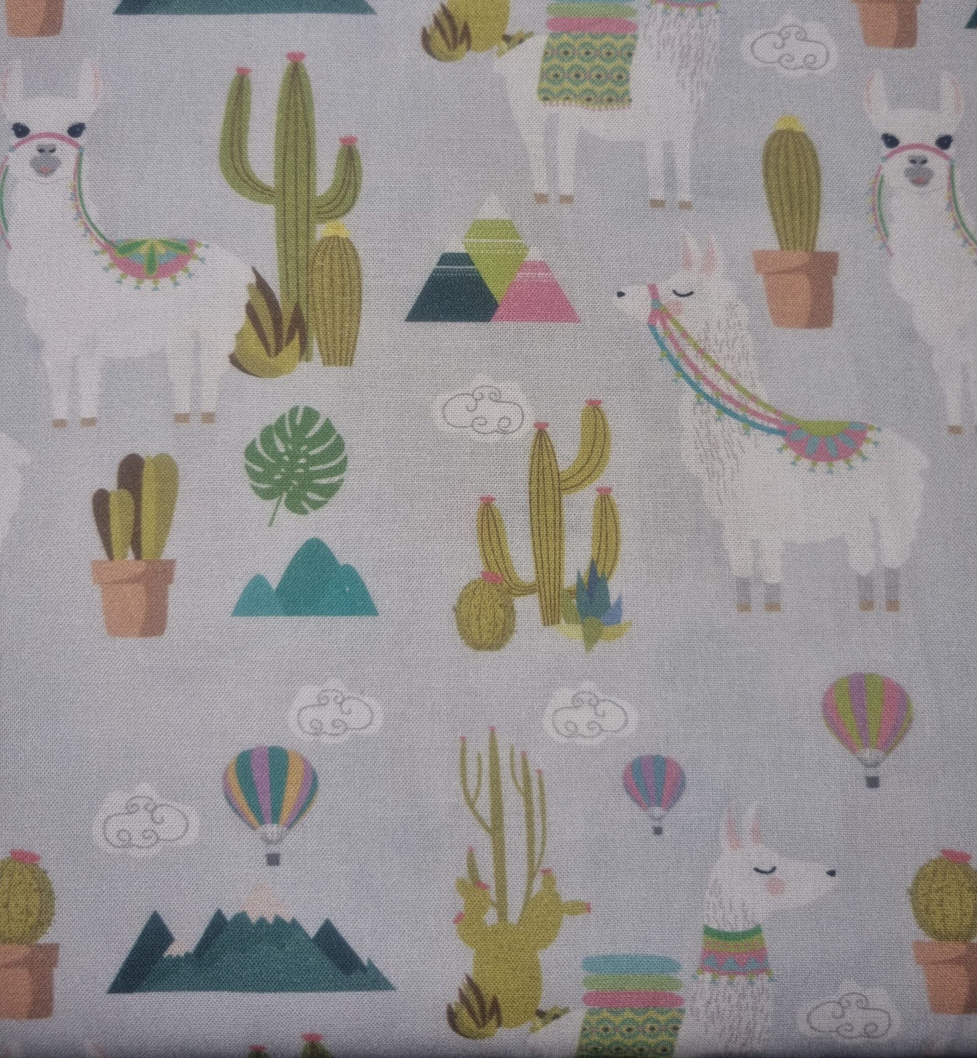 Bright white fabric featuring colourful llamas, cacti, mountains, hot air balloons, and clouds with a whimsical desert and mountain landscape design, ideal for children’s or novelty textiles.
