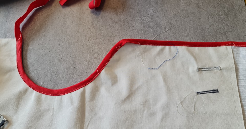 Blue stitching and sewing details on white fabric with red trim, close-up of textile craftsmanship and sewing technique for garment or accessory creation in fabric and finery collection.