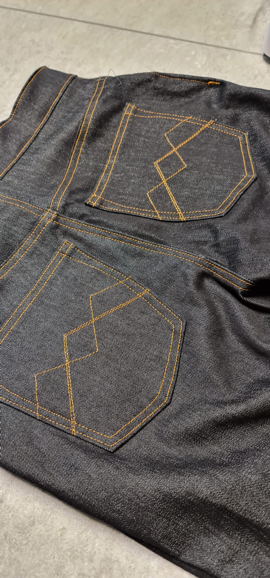Dark denim jeans with yellow contrast stitching and geometric back pocket design.