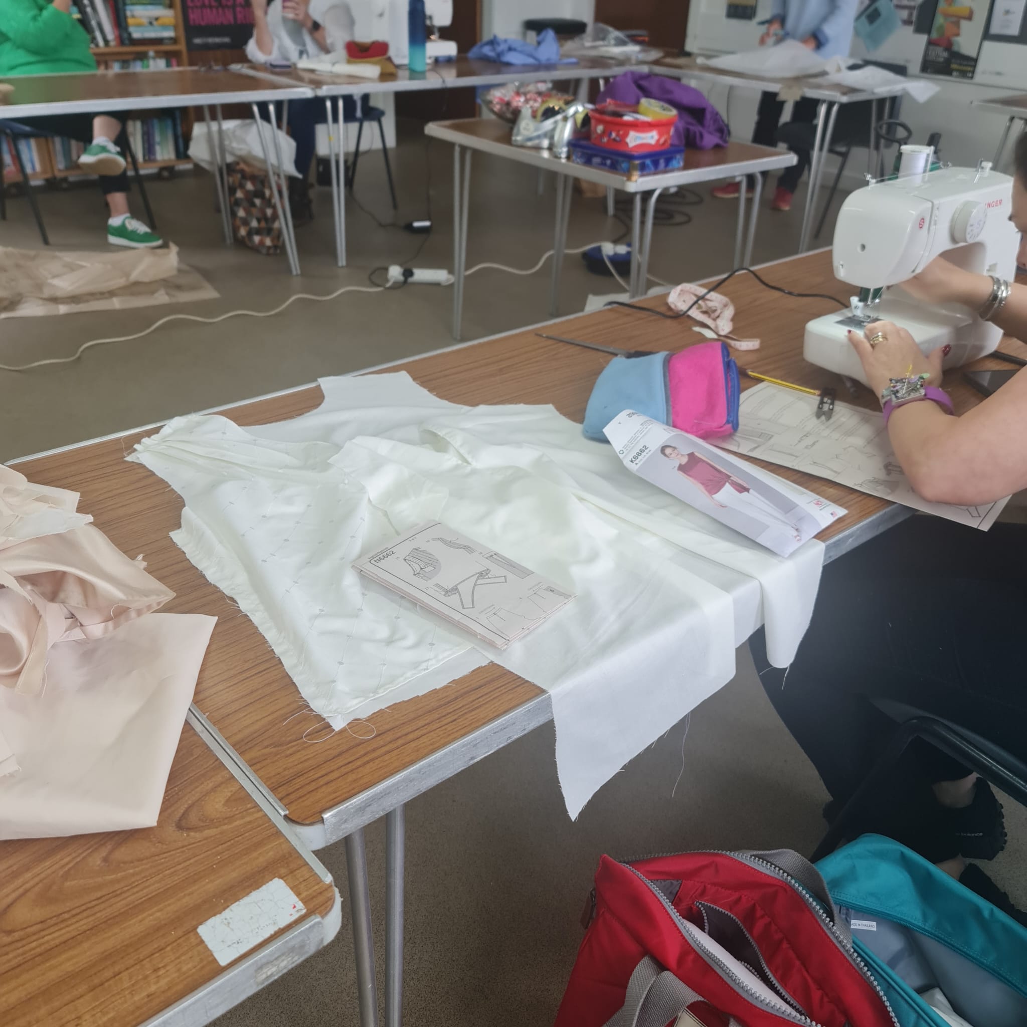 Fresh white fabric and sewing patterns on a work table in a fabric and finery workshop, with sewing machine and crafting supplies, highlighting quality textiles and tailoring education.