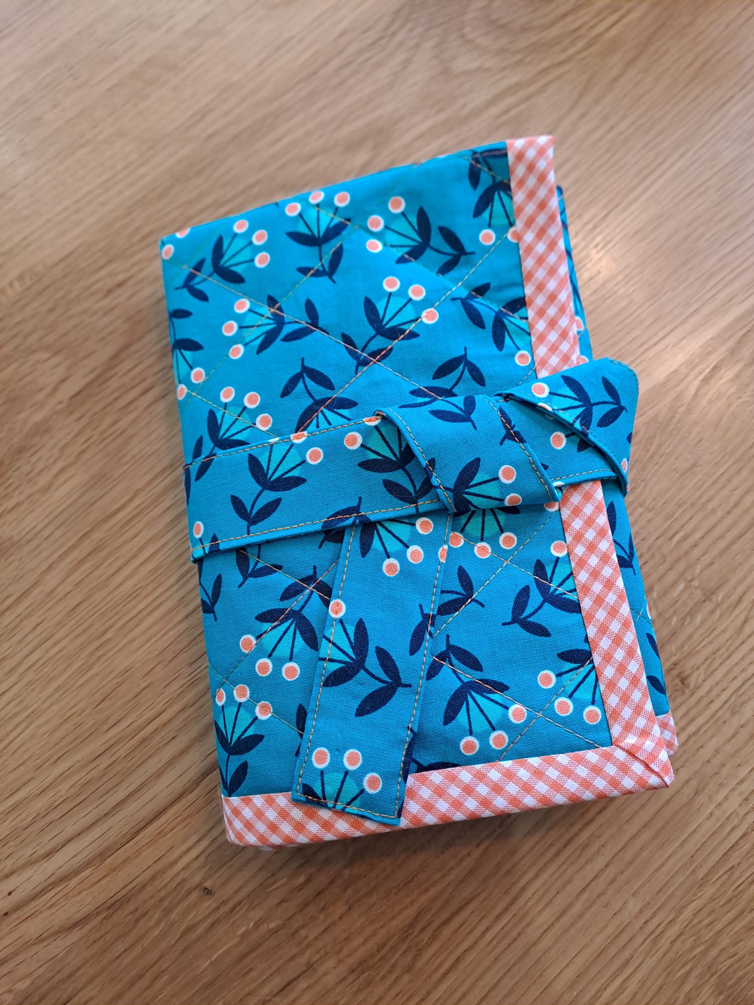 Vibrant blue fabric gift wrap with a floral and berry pattern, featuring a gingham border and a fabric tie, ideal for eco-friendly wrapping in sewing and craft projects.