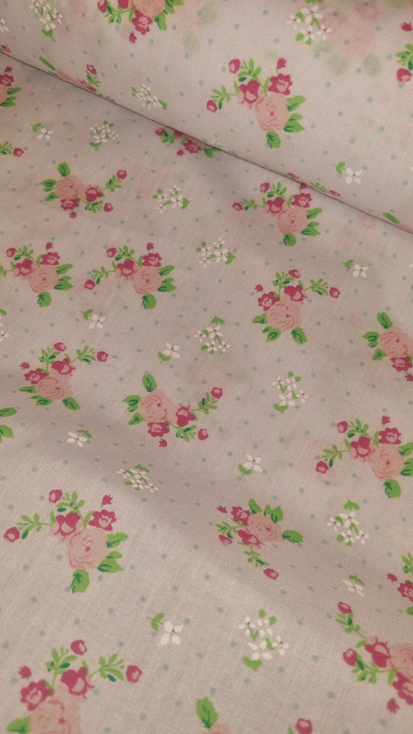 Delicate pink floral fabric with small green leaves and white accents, perfect for sewing projects, quilting, or dressmaking, offering a charming and vintage-inspired aesthetic.