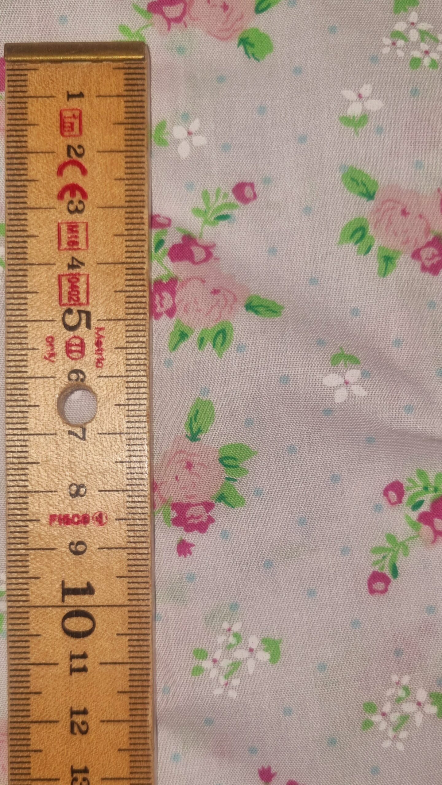 Bright floral fabric with pink roses, green leaves, and white blossoms on a light background, ideal for sewing and fashion projects.