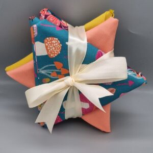 Vibrant fabric bundle with colourful patterns, including floral and abstract designs, tied with a elegant cream satin ribbon, perfect for sewing and quilting projects.