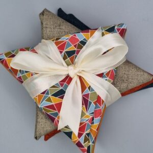 Luxurious fabric and finery gift wrap with colourful geometric patterned fabric, beige linen, and dark navy textiles, accented with a satin ribbon for elegant presentation.