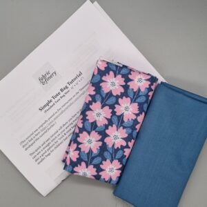 Vibrant floral fabric and plain blue fabric for DIY sewing projects on grey surface with sewing instructions. Perfect for craft, upholstery, and clothing creation, showcasing high-quality textiles from Fabric & Finery.