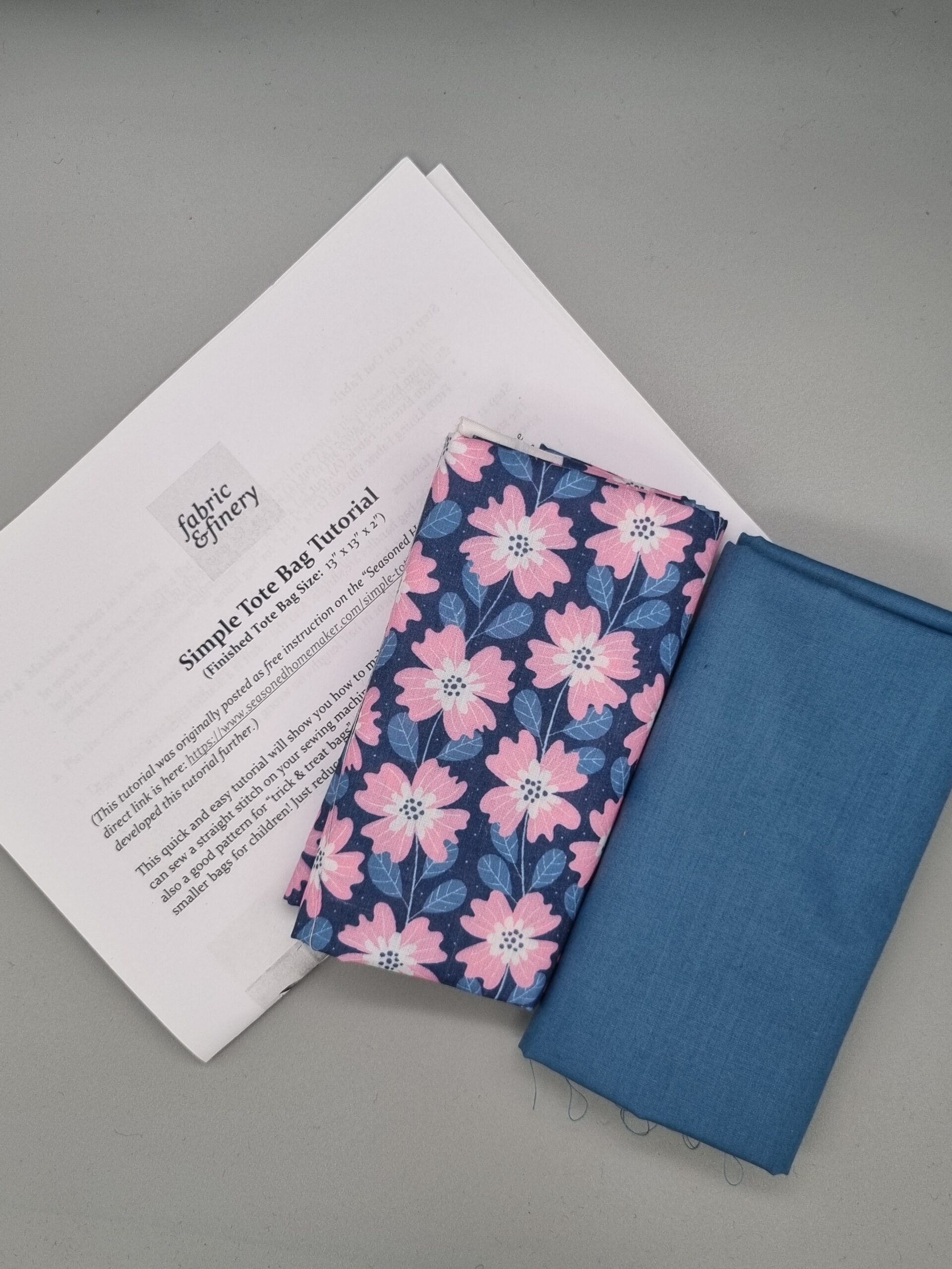 Vibrant floral fabric and plain blue fabric for DIY sewing projects on grey surface with sewing instructions. Perfect for craft, upholstery, and clothing creation, showcasing high-quality textiles from Fabric & Finery.