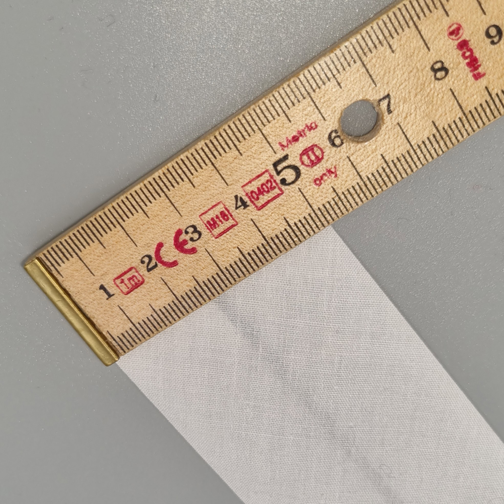 Soft white fabric swatch for sewing and dressmaking, displayed alongside a wooden ruler measuring fabric width, perfect for craft projects, fashion design, and bespoke clothing creation.
