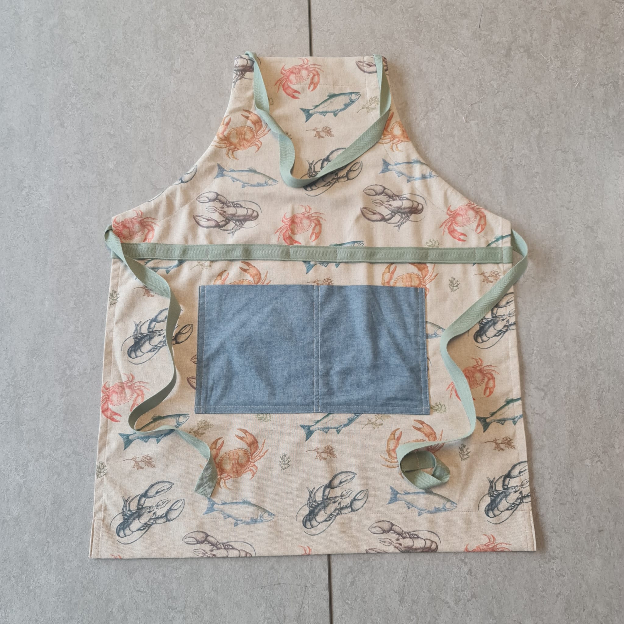Crab and fish-themed apron made from high-quality fabric, featuring a front pocket and adjustable straps, ideal for cooking or crafting with a stylish ocean-inspired design.