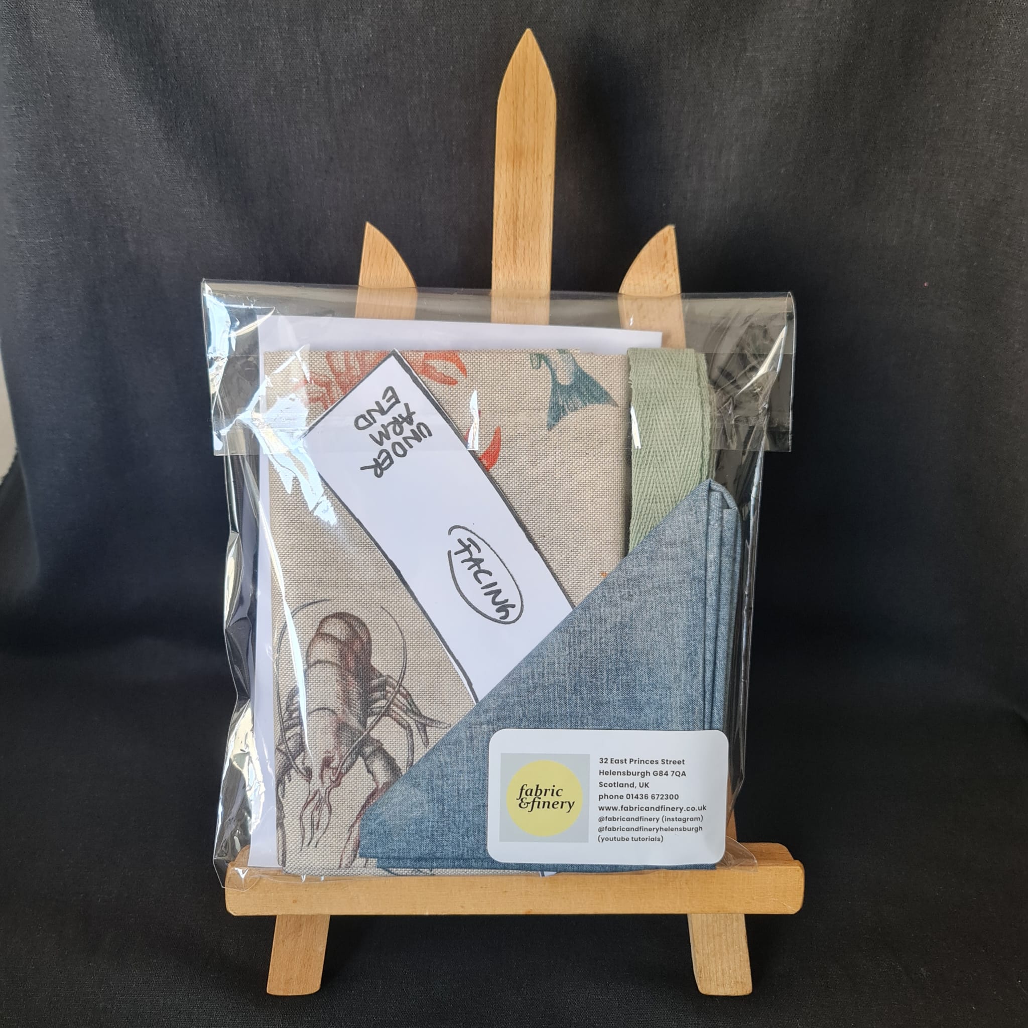 Soft fabric samples in a clear packaging with a lobster illustration, featuring botanical prints and solid colours, ideal for bespoke sewing and interior design projects.