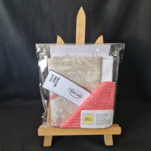 Aesthetic fabric sample set with embroidery, patterned, and plain textiles, presented in a clear plastic bag on a small wooden stand, perfect for sewing, quilting, and craft projects.