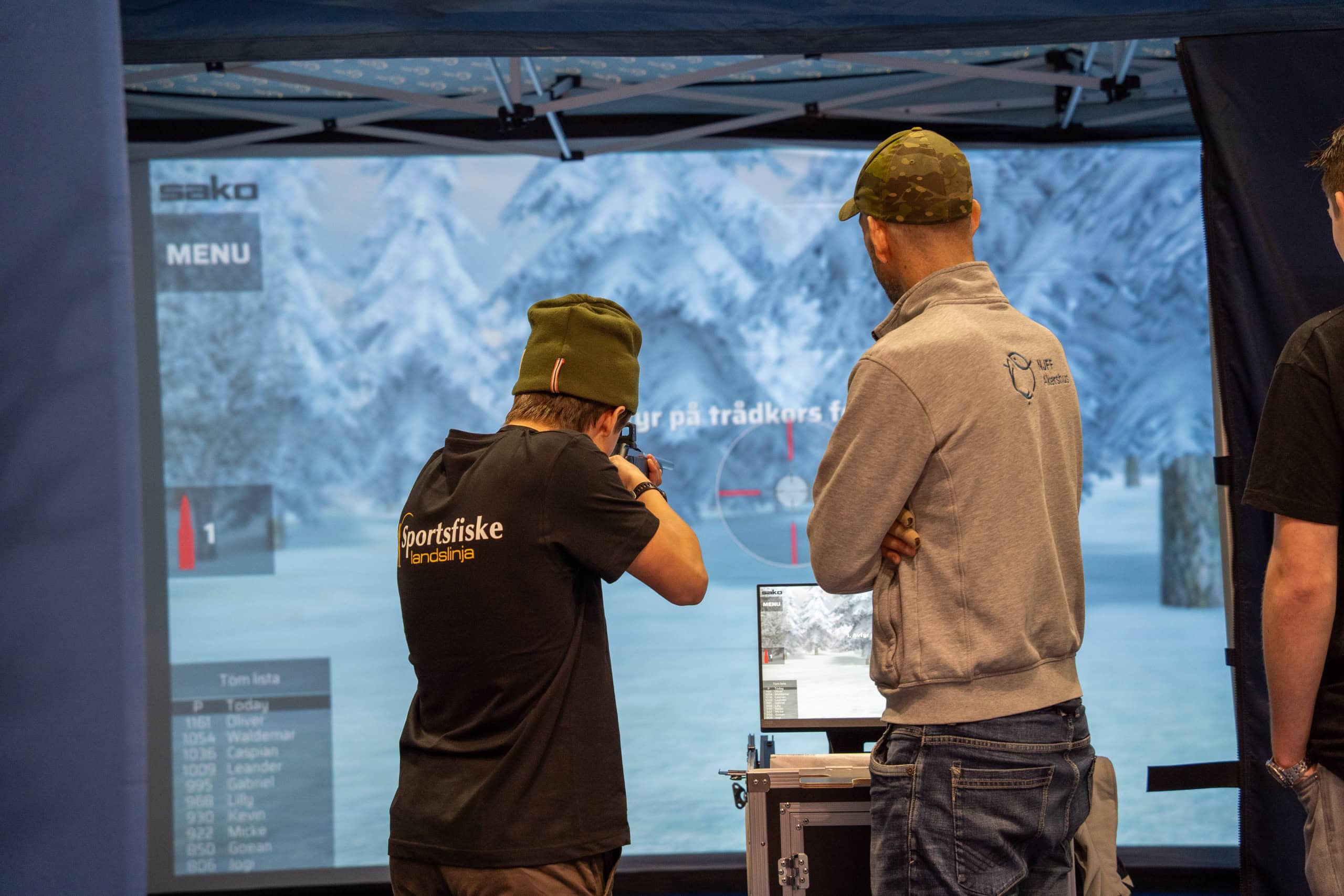 To personer som viser en digital skjerm under en utendørs messe i snølandskapet.