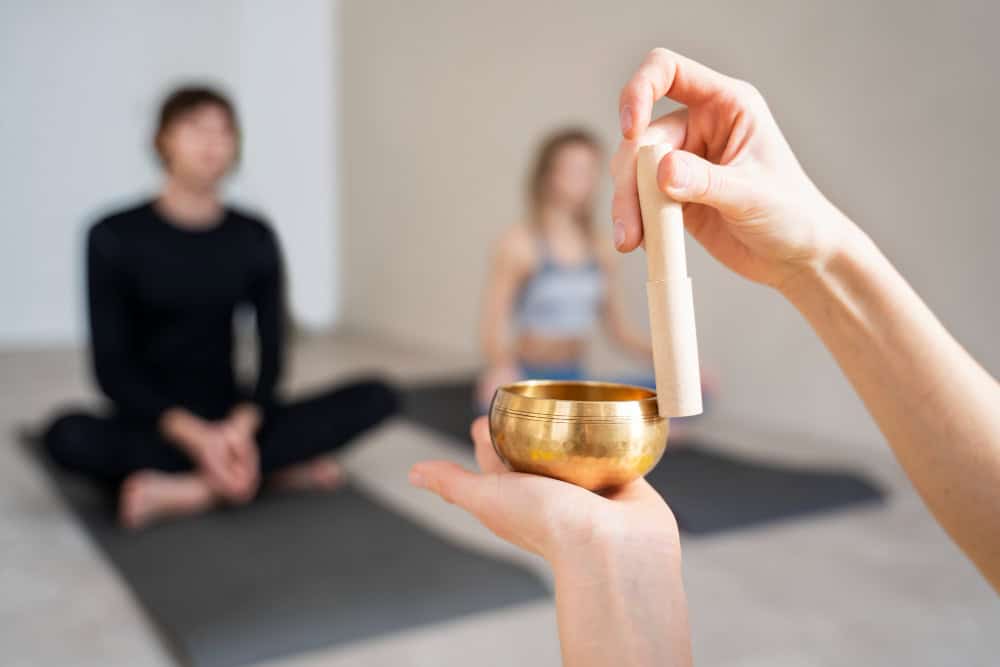 Sessione di meditazione con campana tibetana e mazzo di tamburi, con due persone sedute in posizione di meditazione in un ambiente tranquillo e luminoso.