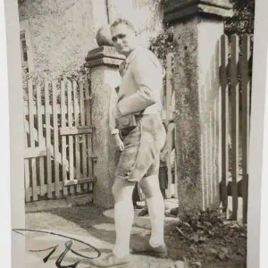 Vintage black and white photo of a man standing outdoors near a fence and stone pillars.