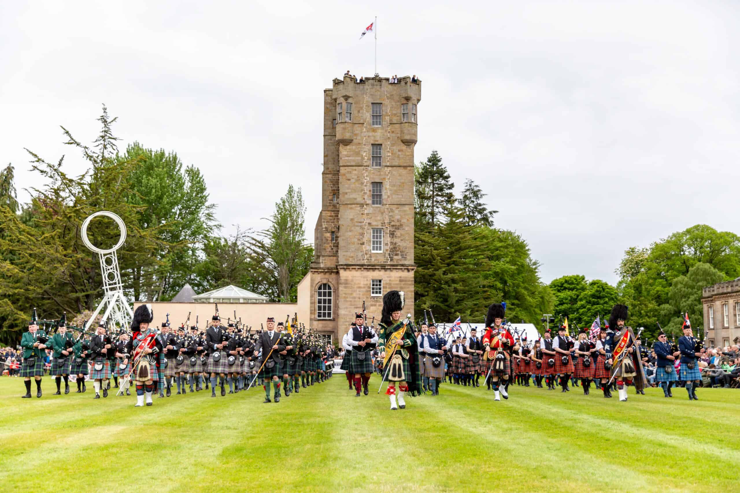 Mass pipe band parade at Gordon Castle Highland Games in front of the tower