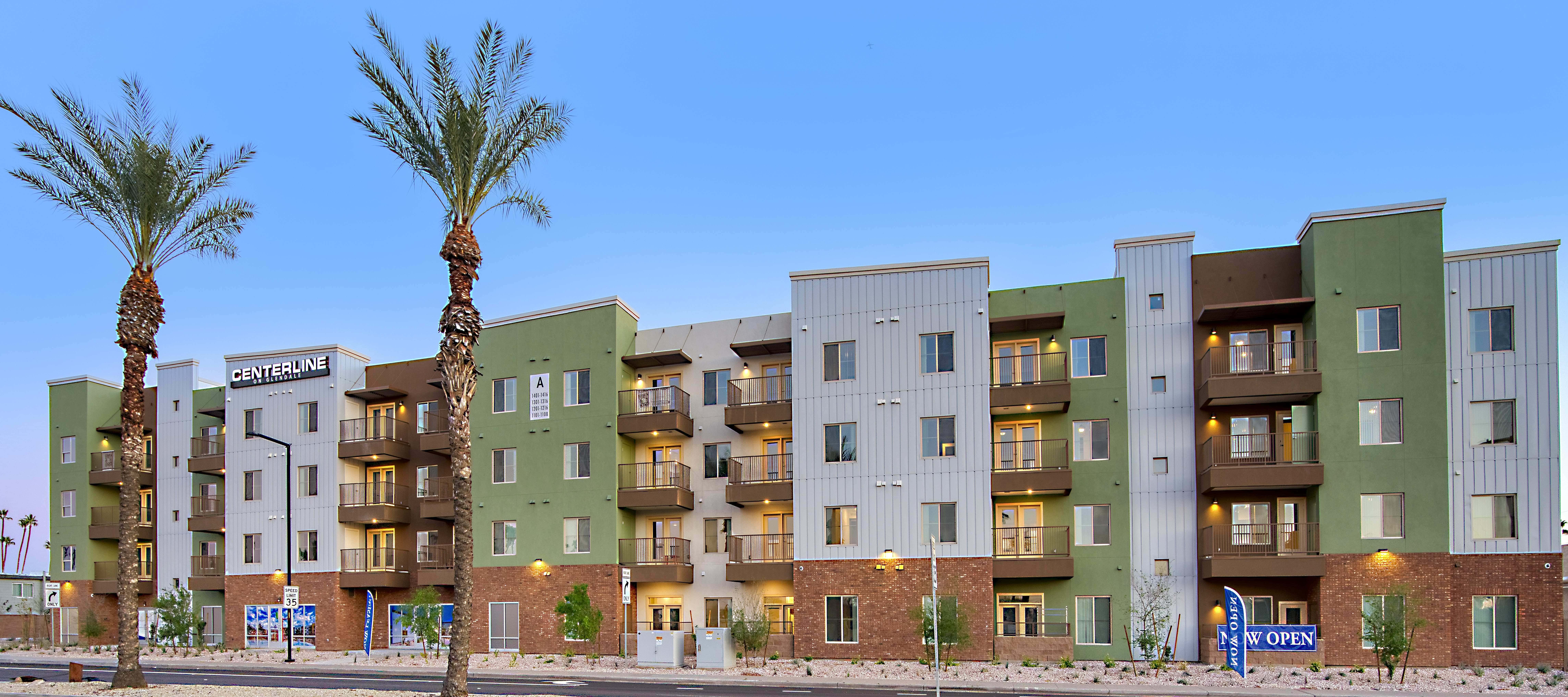 Modern multi-family residential building with green and white exterior, balconies, and palm trees.