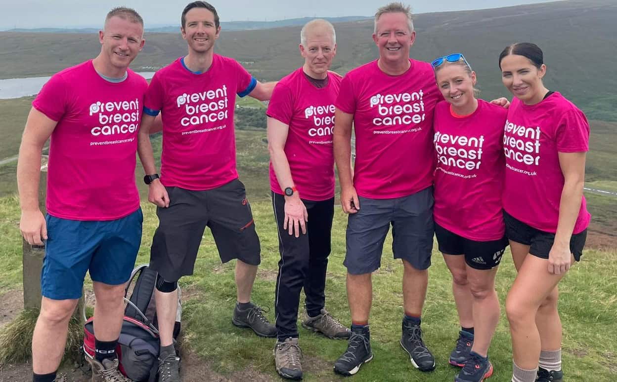 Prevent breast cancer charity group wearing pink T-shirts outdoors in a rural landscape, supporting breast cancer awareness and fundraising.