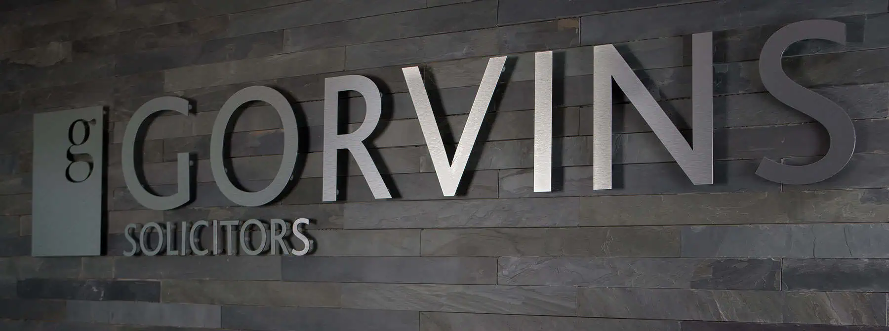 Modern dark grey stone wall with large metallic "Gorvins" and "Solicitors" sign, showcasing professional legal office branding and contemporary interior design.