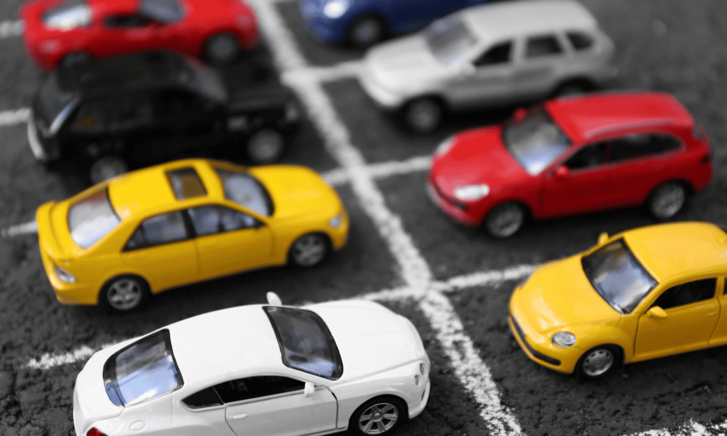 A variety of colourful cars parked in a parking lot with white lines marking the spaces.