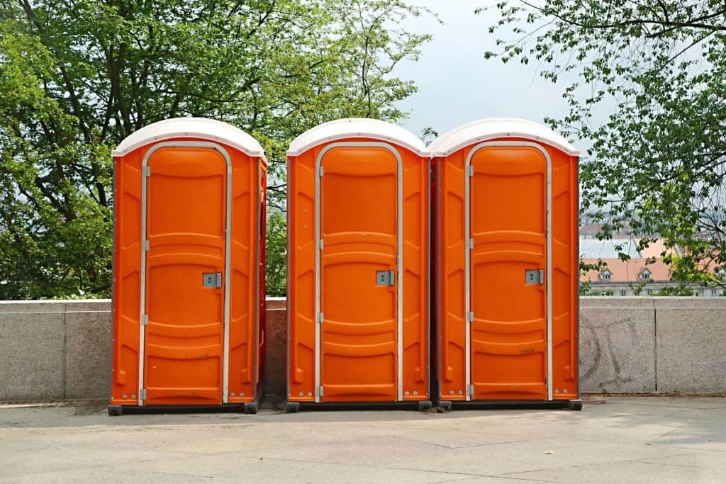 Three orange portable restrooms lined up outdoors for event use.
