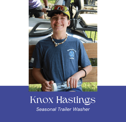 Young boy smiling with a water bottle outdoors, wearing a blue shirt and cap.