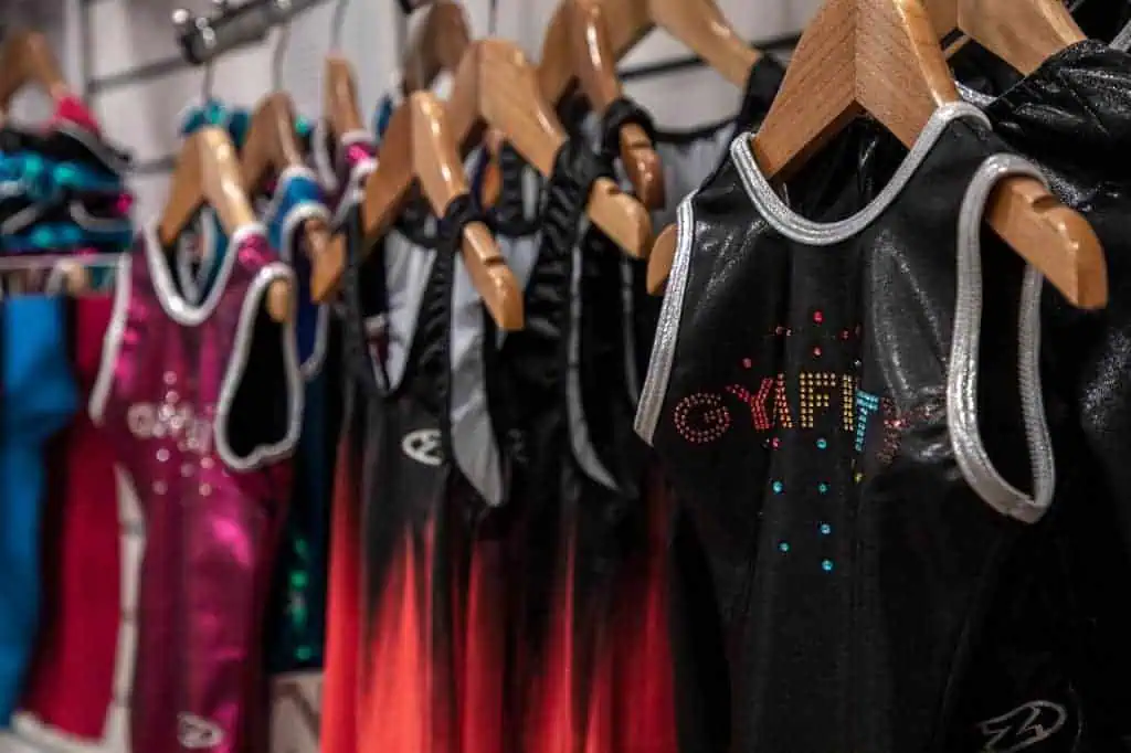 Brightly coloured cheerleading costumes hanging on wooden hangers in a sportswear store.