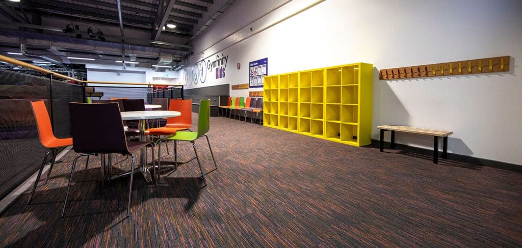 Bright play area in a children's gym with colourful chairs, storage units, and hooks for hanging coats or bags, providing a fun and organised space for kids.