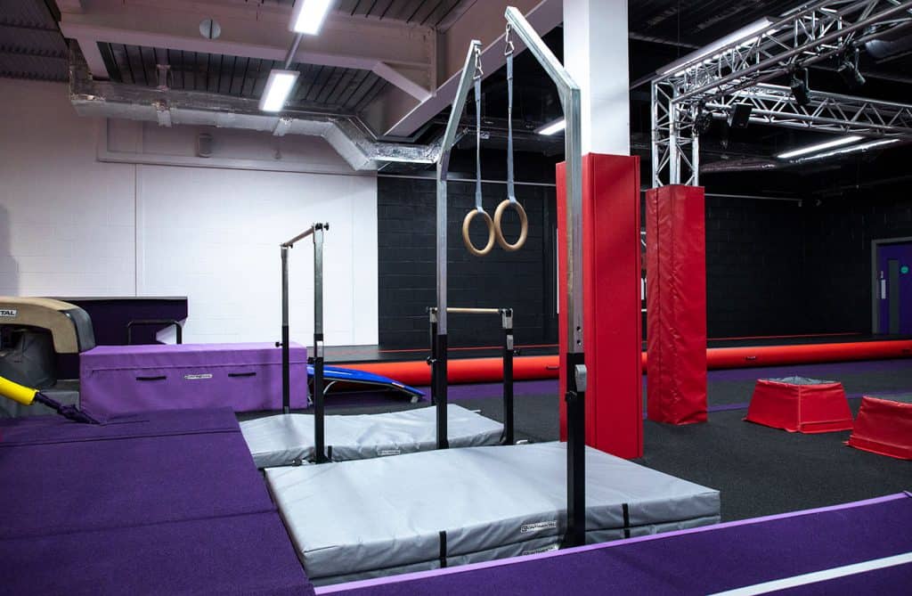 Climbing gym with gymnastic rings, padded areas, and gym equipment for strength and agility training. Modern indoor fitness space designed for general and specialized workouts.